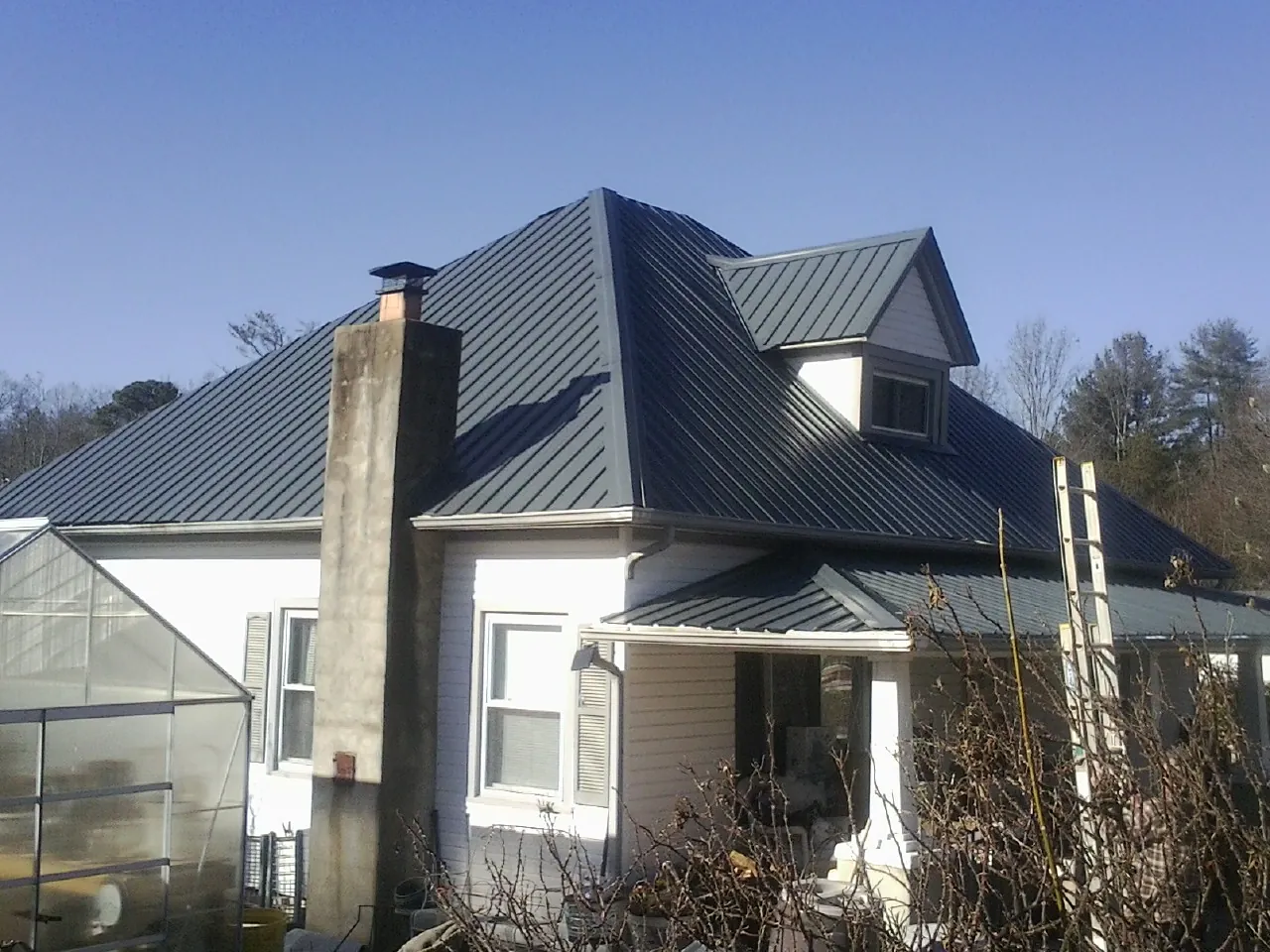 Dark blue standing seam metal roof on a white farmhouse with dormer — Slate & Tile Roof Repair by Roofing Brothers in Francis Creek