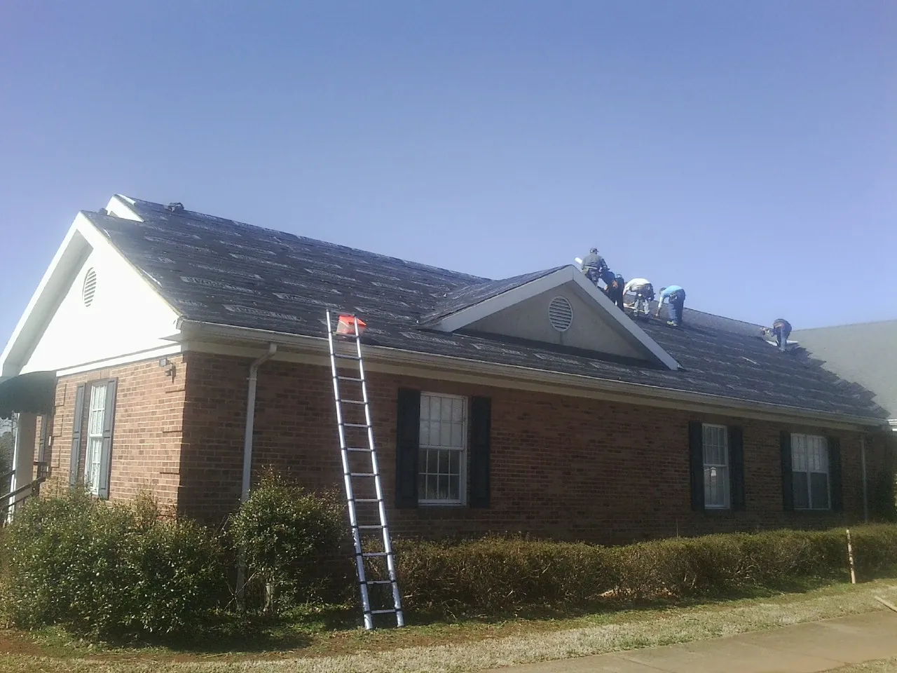 Crew tearing shingles off a brick ranch roof with a ladder set — Emergency Roof Repair work by our crew in Francis Creek