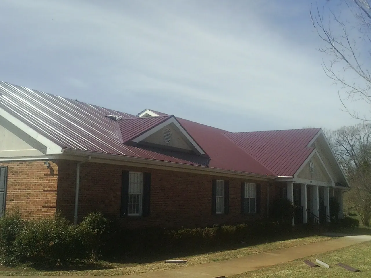 Red metal roof with gabled entries on a long brick building, from a Hail Damage Roof Repair job in Francis Creek