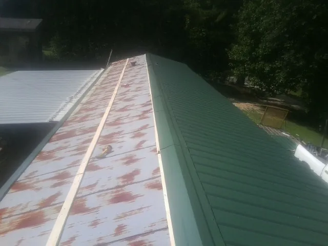 Old rusted panels beside newly installed green metal roofing — Wind Damage Roof Repair by Roofing Brothers in Francis Creek