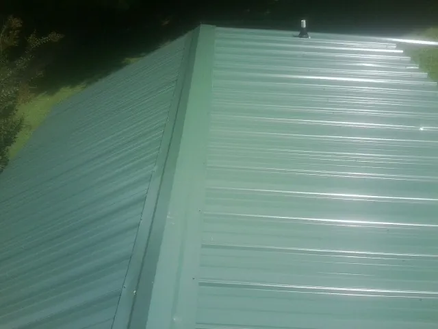 New green metal panels meeting at the ridge of a roof — Flat Roof Repair work by our crew in Francis Creek