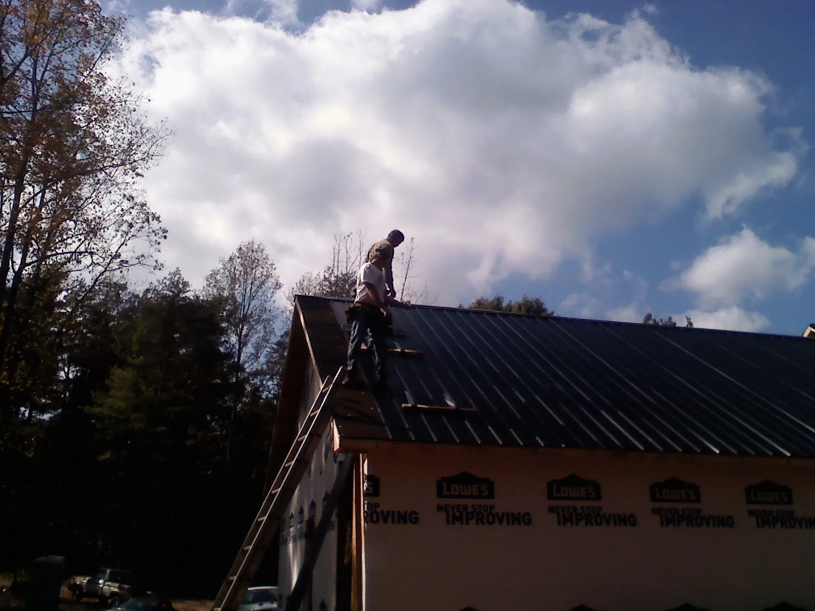 Roofer fastening dark metal panels high against a cloudy sky, from a Roof Inspection job in Francis Creek