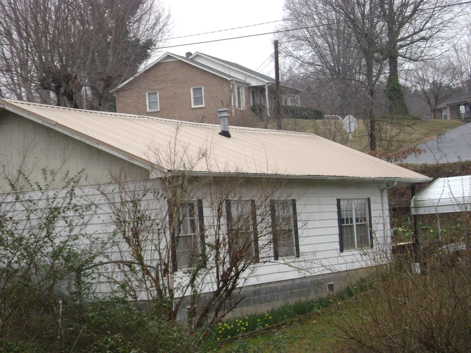 Tan metal roof on a white sided house set into a hillside — Commercial Roofing by Roofing Brothers in Francis Creek