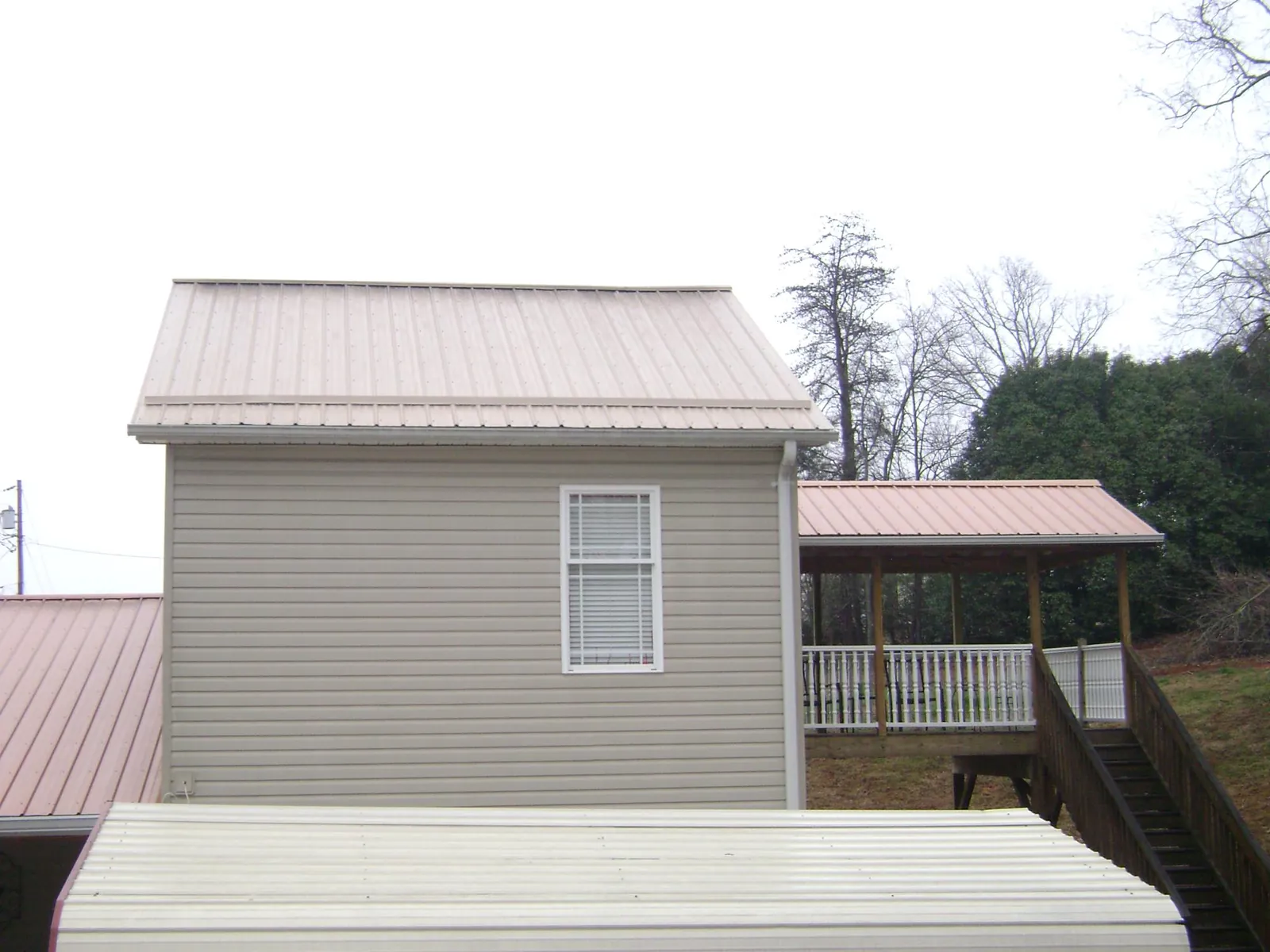 Tan metal roofs on a two story addition and attached porch, from a Roof Replacement job in Francis Creek